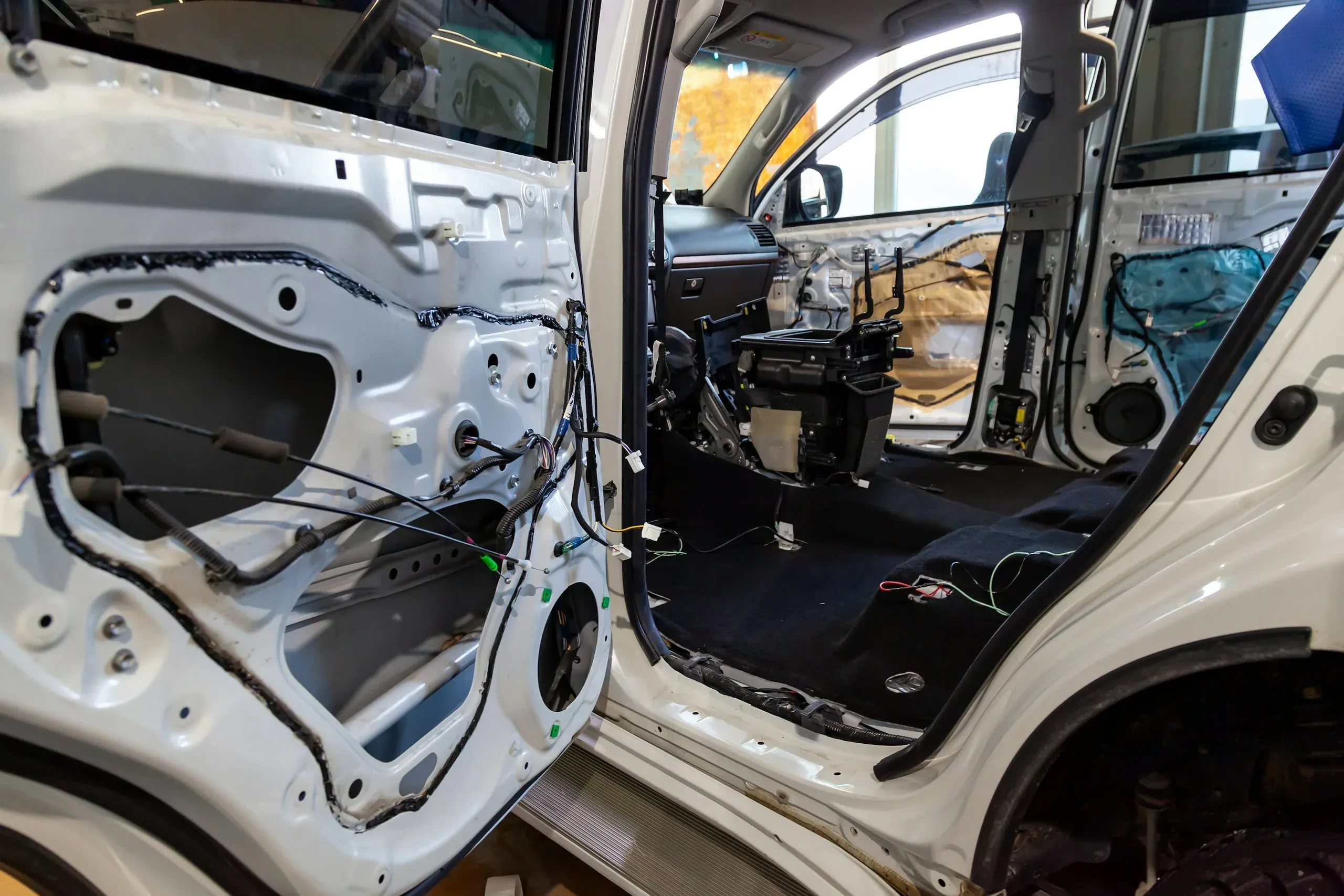 Car body in a workshop with the front door open, showing the inner door panel, wiring and cabin structure