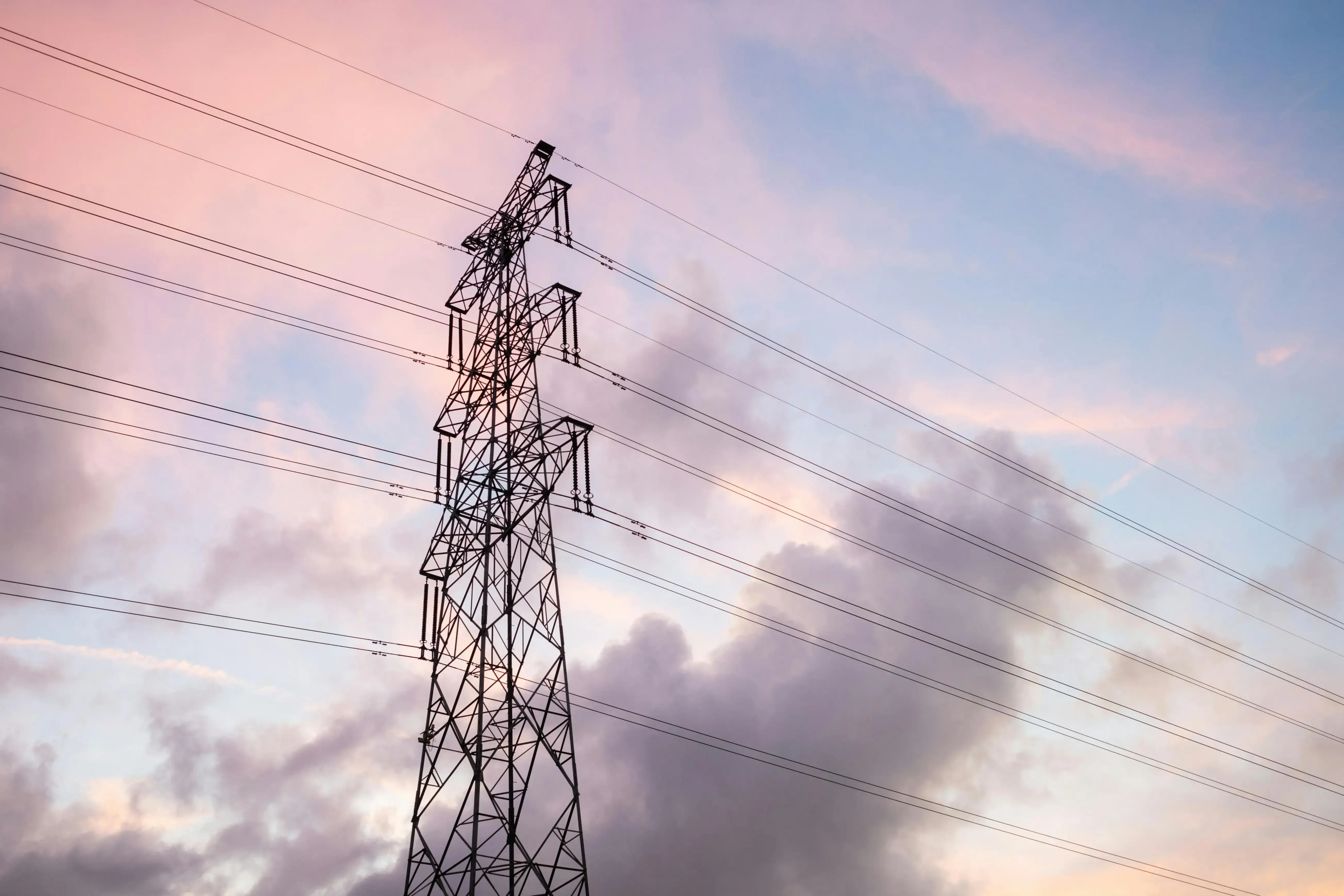 Steel lattice transmission tower against a pink sky